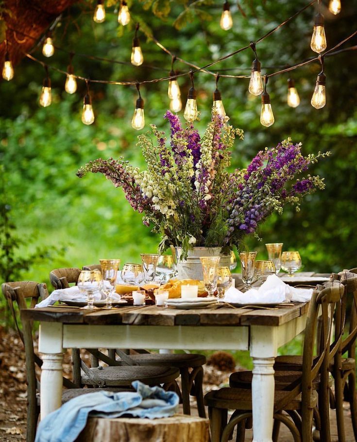 an outdoor table set with food and wine glasses on it, surrounded by greenery