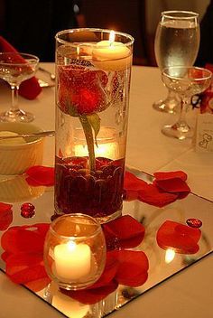 a table topped with candles and flowers on top of a glass plate covered in water