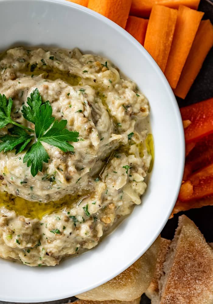 a white bowl filled with dip surrounded by carrots and bread