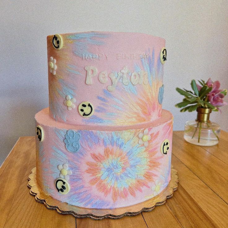 a three tiered cake decorated with flowers and smiley faces on the side, sitting on top of a wooden table