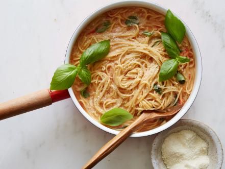 a white bowl filled with pasta and basil on top of a marble counter next to a wooden spoon