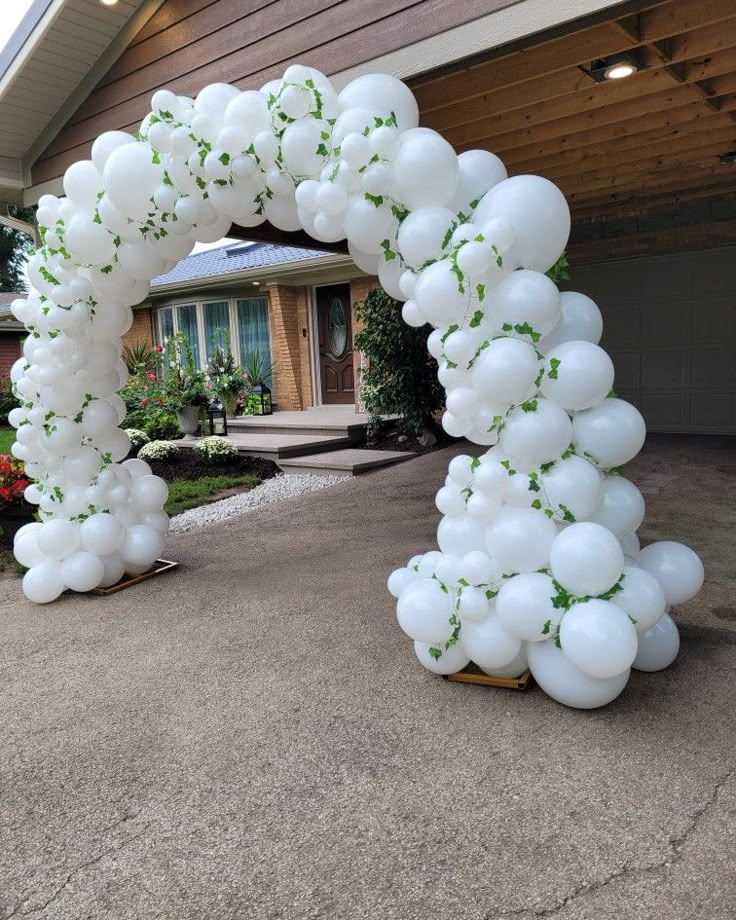 an arch made out of balloons with green leaves on it in front of a house