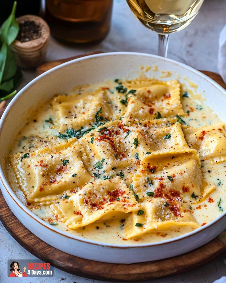 a white bowl filled with ravioli next to a glass of wine