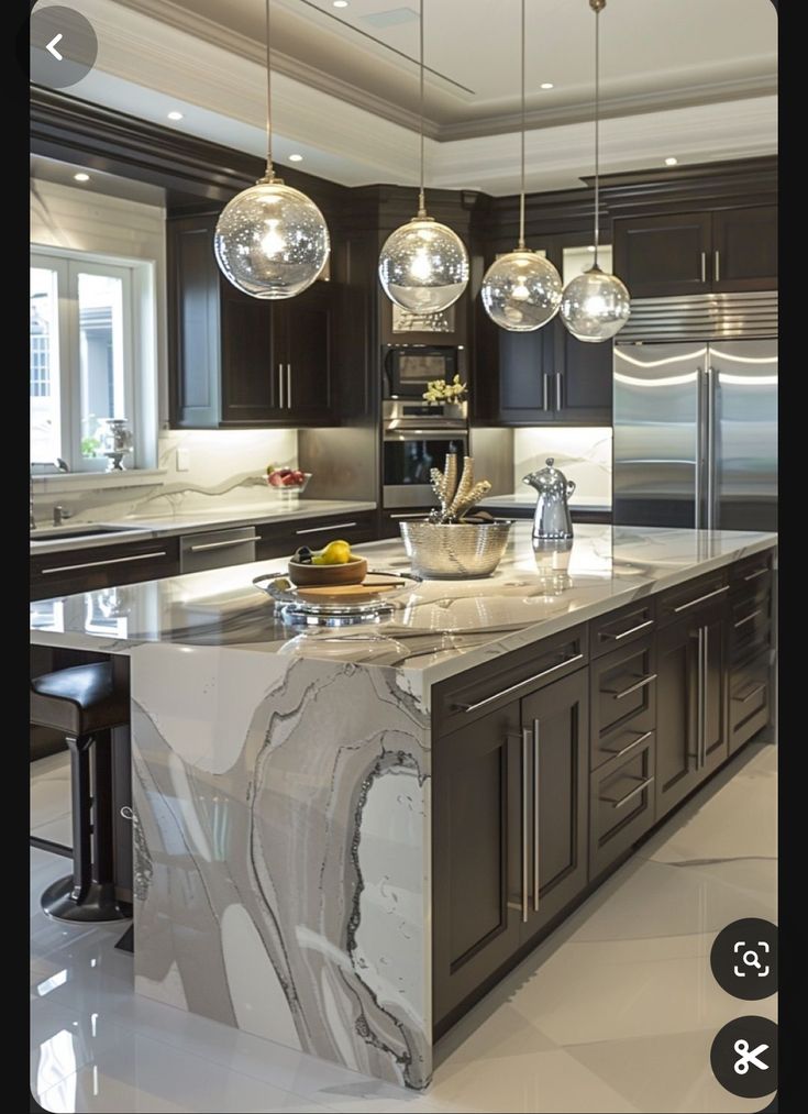 a large kitchen with marble counter tops and stainless steel appliances, along with pendant lights hanging from the ceiling