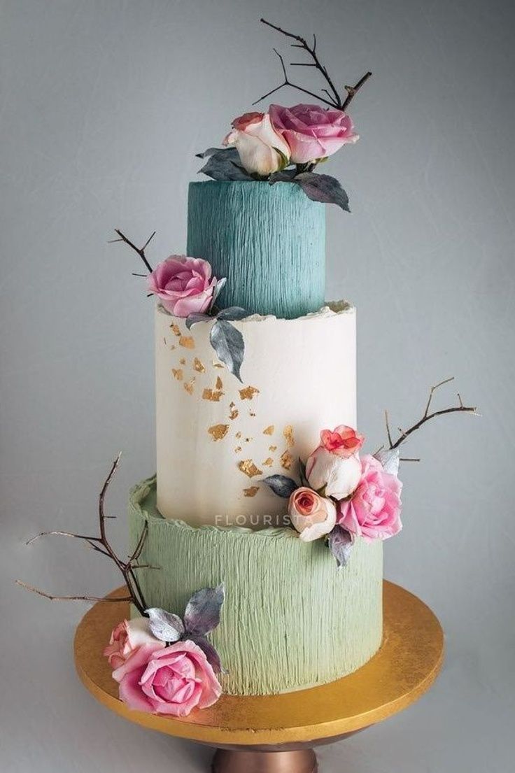 a three tiered cake decorated with flowers and leaves on a gold plated stand