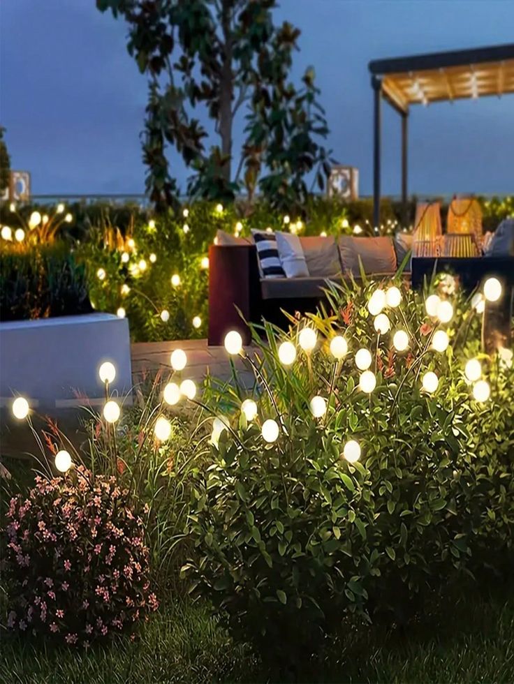 some lights that are in the grass near bushes and flowers on a patio at night