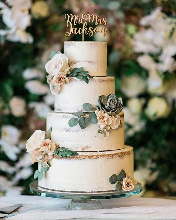 a three tiered cake with flowers on it and greenery in the back ground