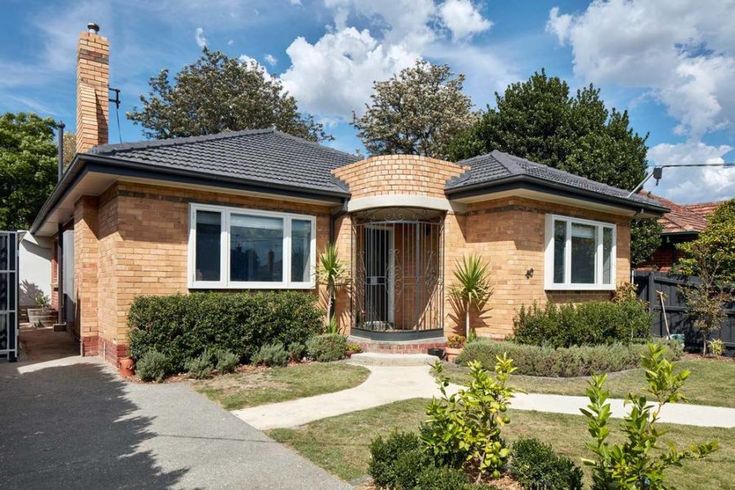 a small brick house with bushes and trees in the front yard