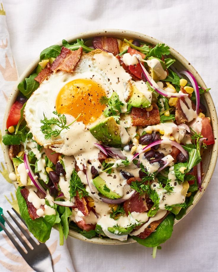 a salad with bacon, lettuce and an egg on top is served in a bowl