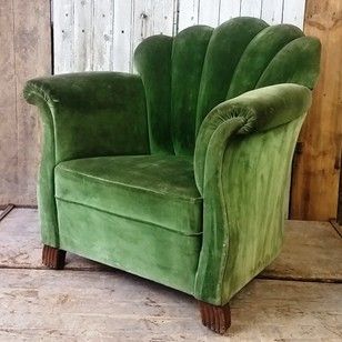 a green velvet chair sitting in front of a wooden wall with peeling paint on it