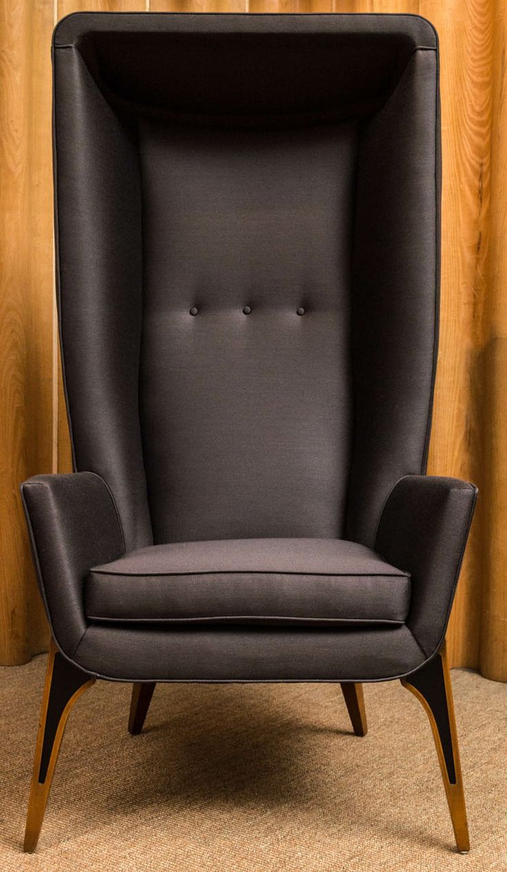 a black leather chair sitting in front of a wooden paneled wall with curtains behind it