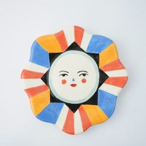 a ceramic plate with a face painted on it's side and an orange, white, blue, and red design