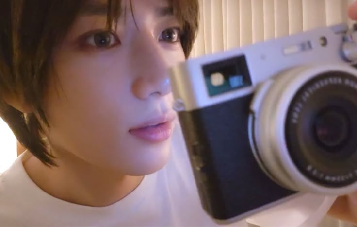 a woman taking a selfie with a camera in front of her face and wearing a white t - shirt