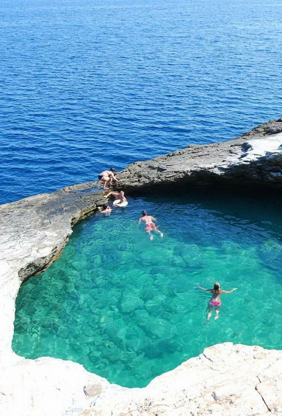 people are swimming in the water near some rocks