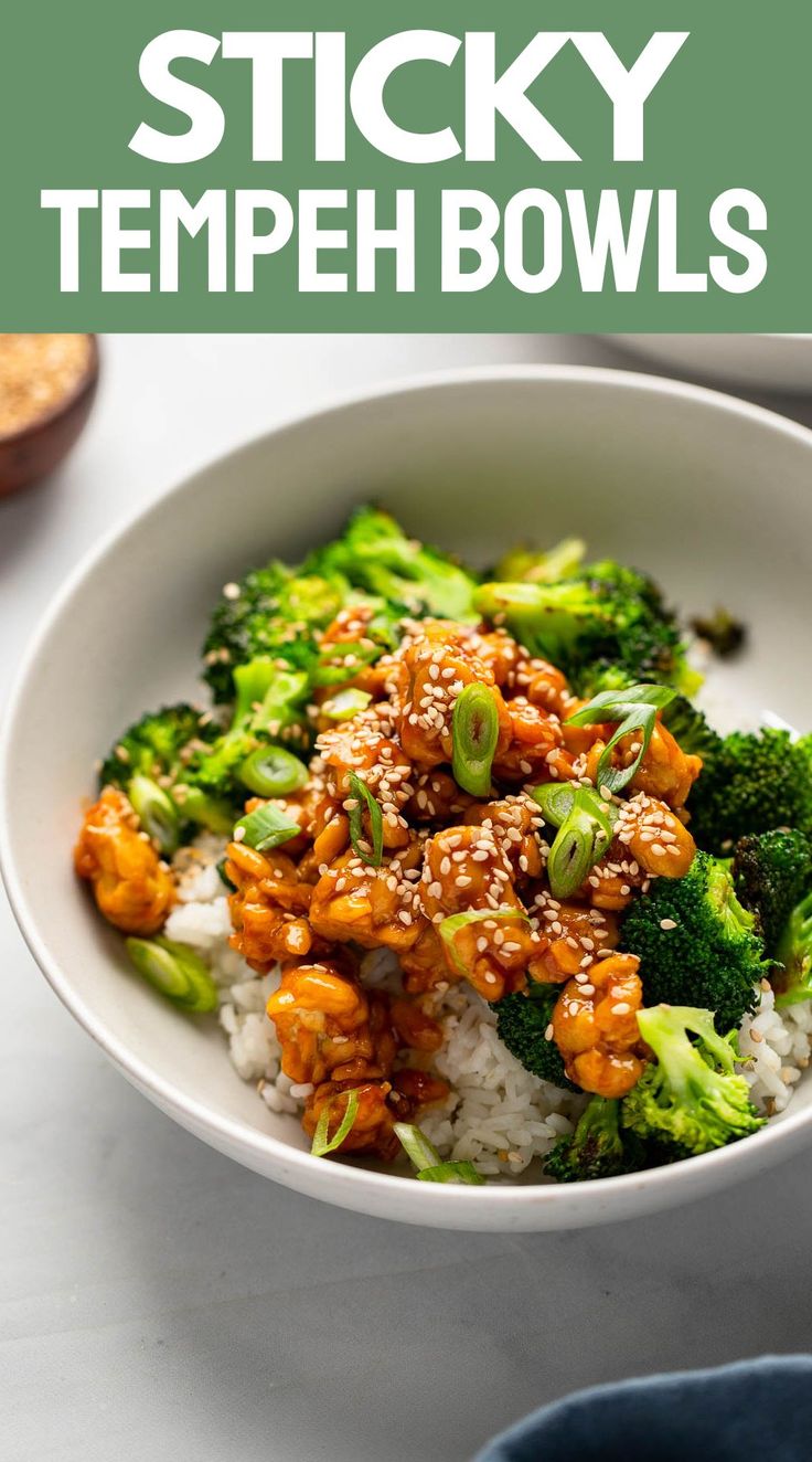 a white bowl filled with rice and broccoli covered in sesame seeds, topped with chicken