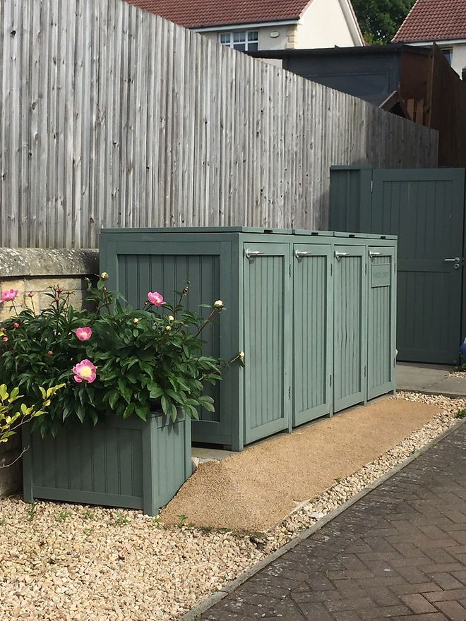 two green storage containers sitting next to each other on the side of a road with flowers growing out of them