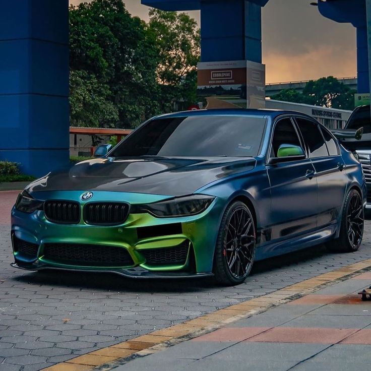 a green and black car parked on the side of a road next to a building