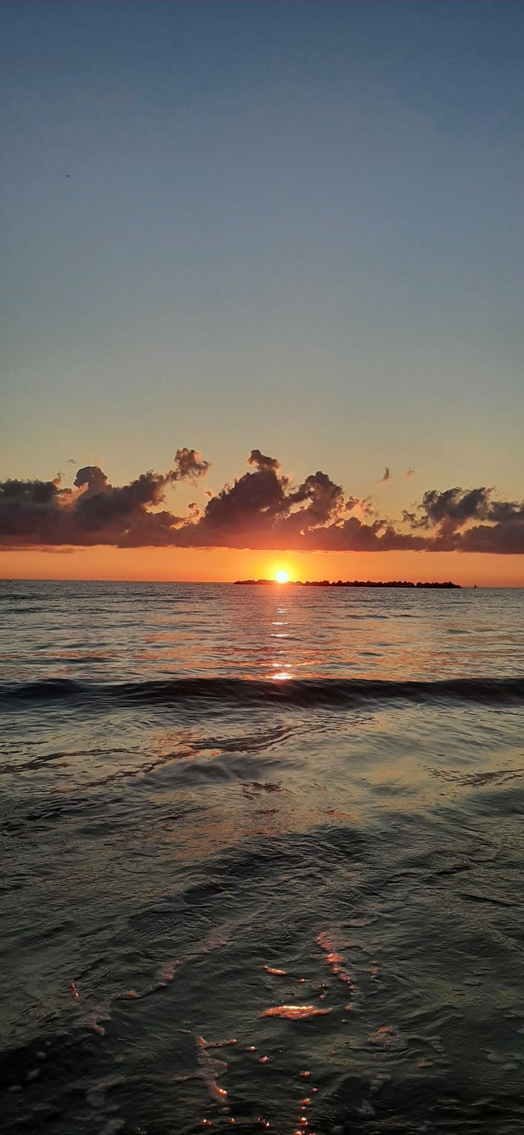 the sun is setting over the ocean with clouds in the sky and water below it