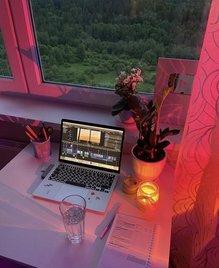 an open laptop computer sitting on top of a desk next to a plant and candle