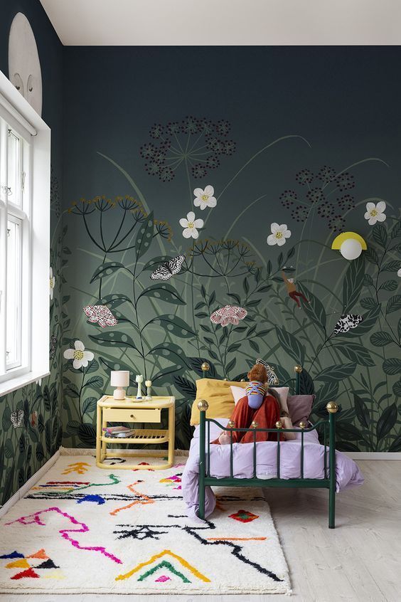 a person sitting on a bed in front of a wall with flowers painted on it