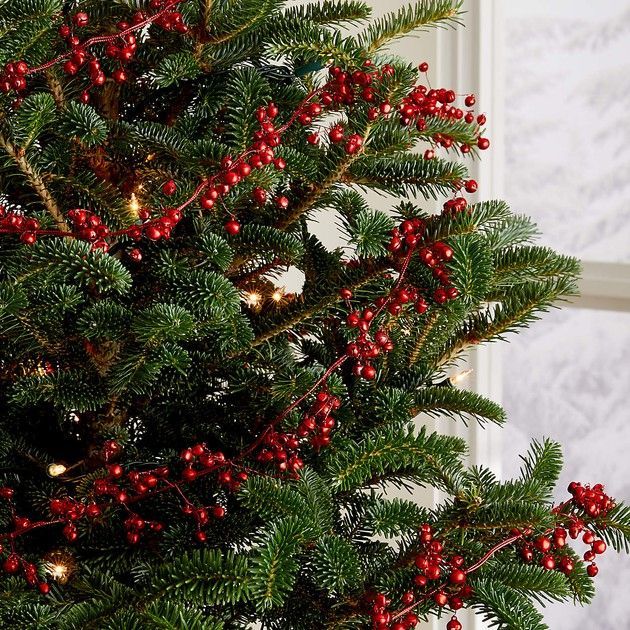 a close up of a christmas tree with red berries and green leaves in front of a window