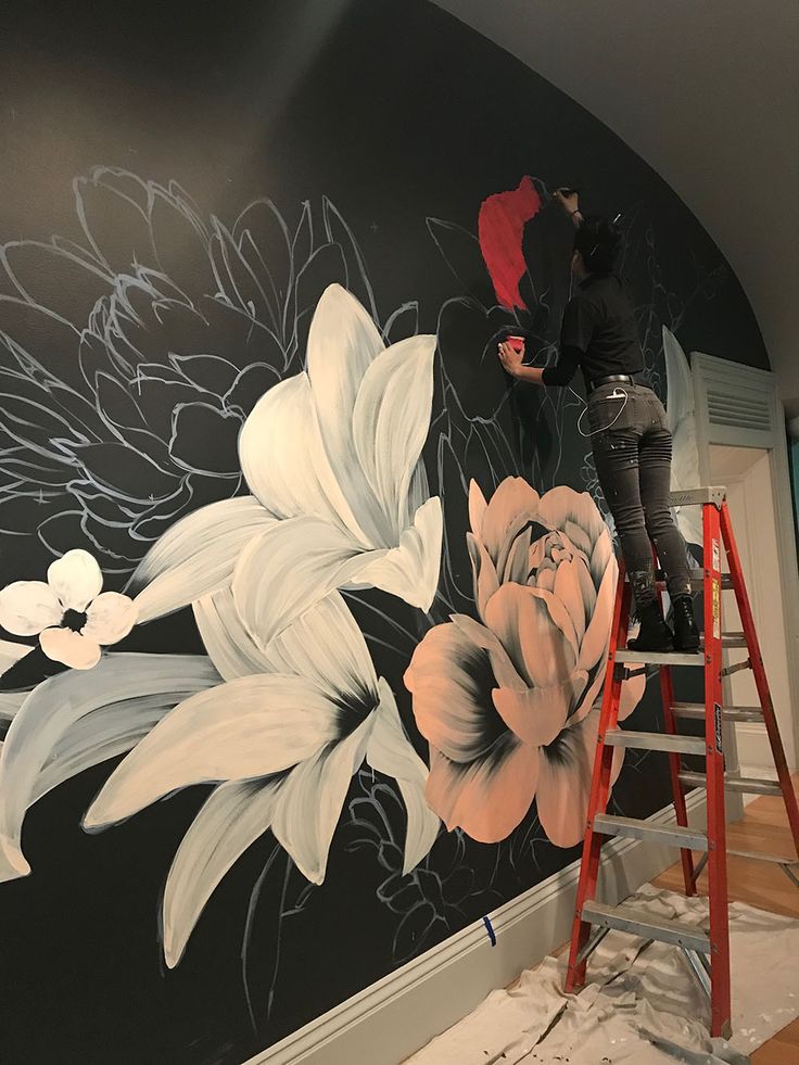 a man on a ladder painting a wall with flowers