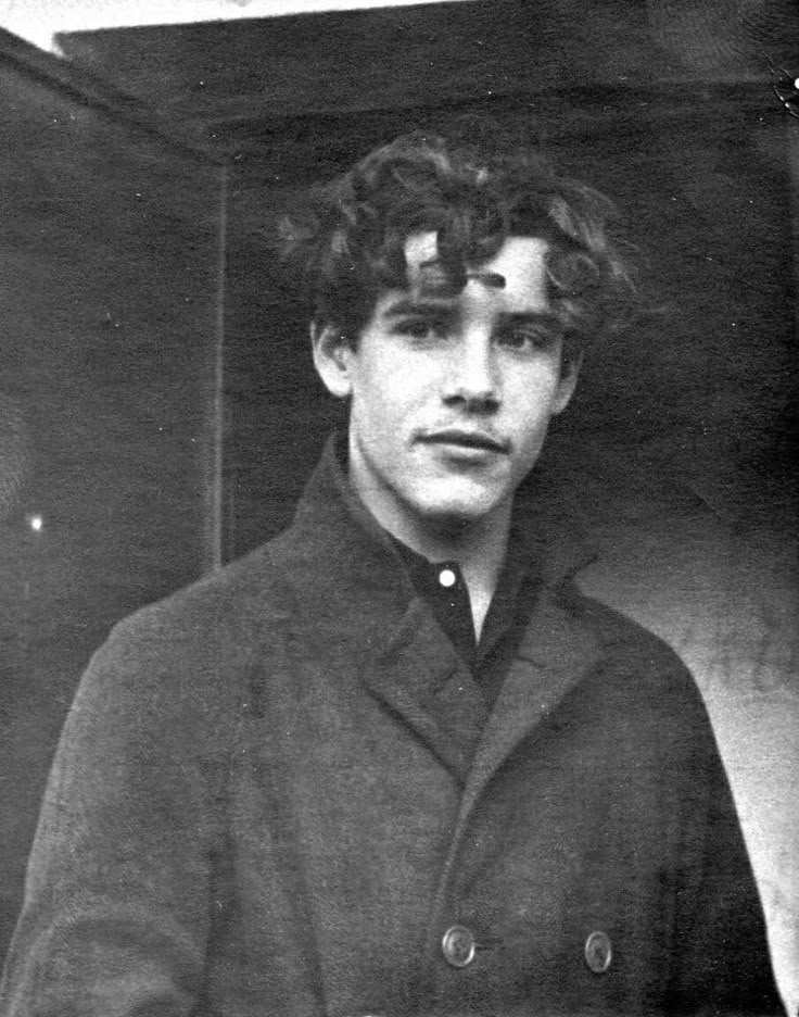 an old black and white photo of a young man in a coat looking at the camera