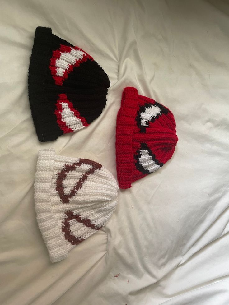 three knitted hats laying on top of a white bed next to an unmade pillow