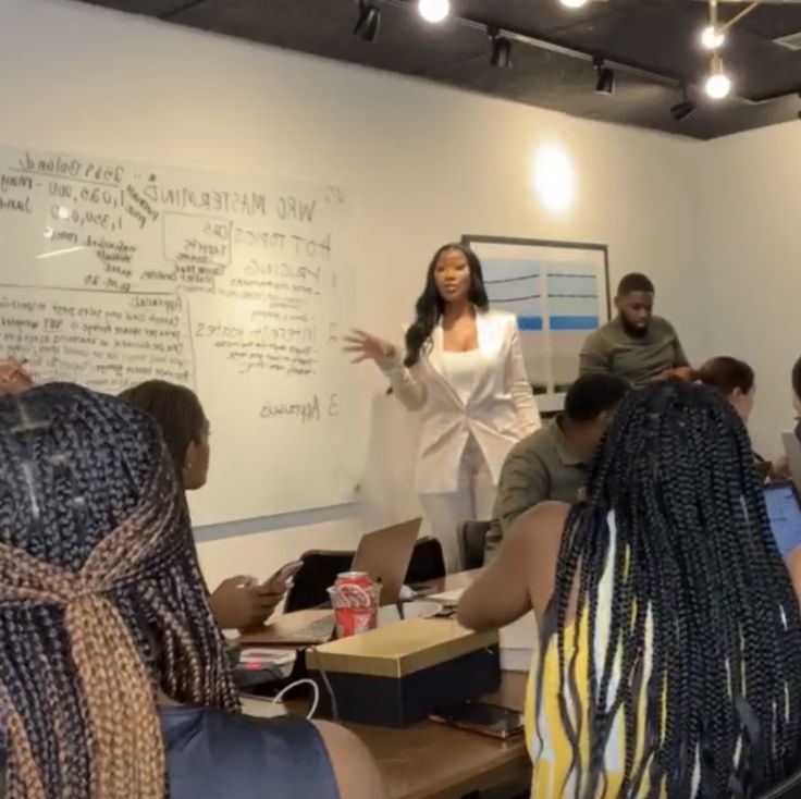 a group of people sitting at desks in front of a whiteboard with writing on it