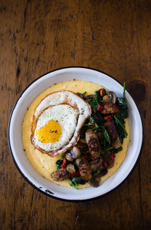 a white plate topped with grits and an egg on top of spinach leaves