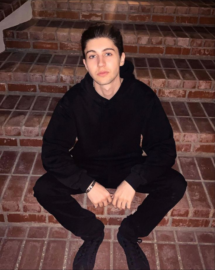 a young man sitting on the steps in front of some brick stairs with his hands crossed