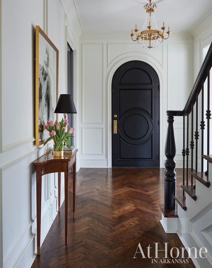 an entry way with a black door and wooden flooring in front of a chandelier