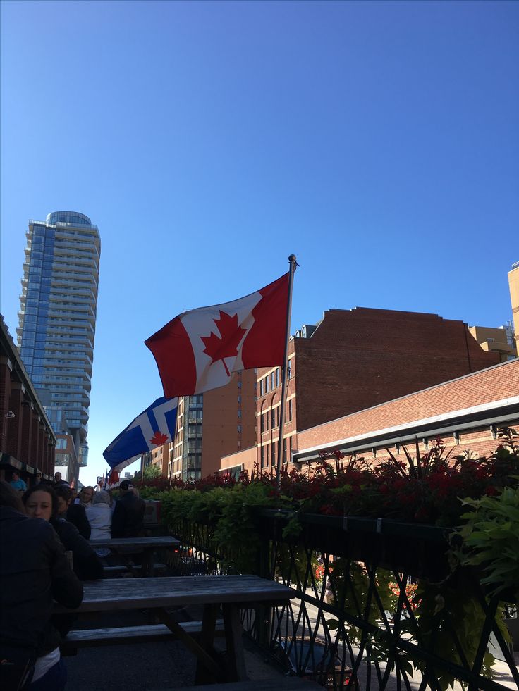 the canadian and canadian flags are flying high in the sky above some buildings on a sunny day