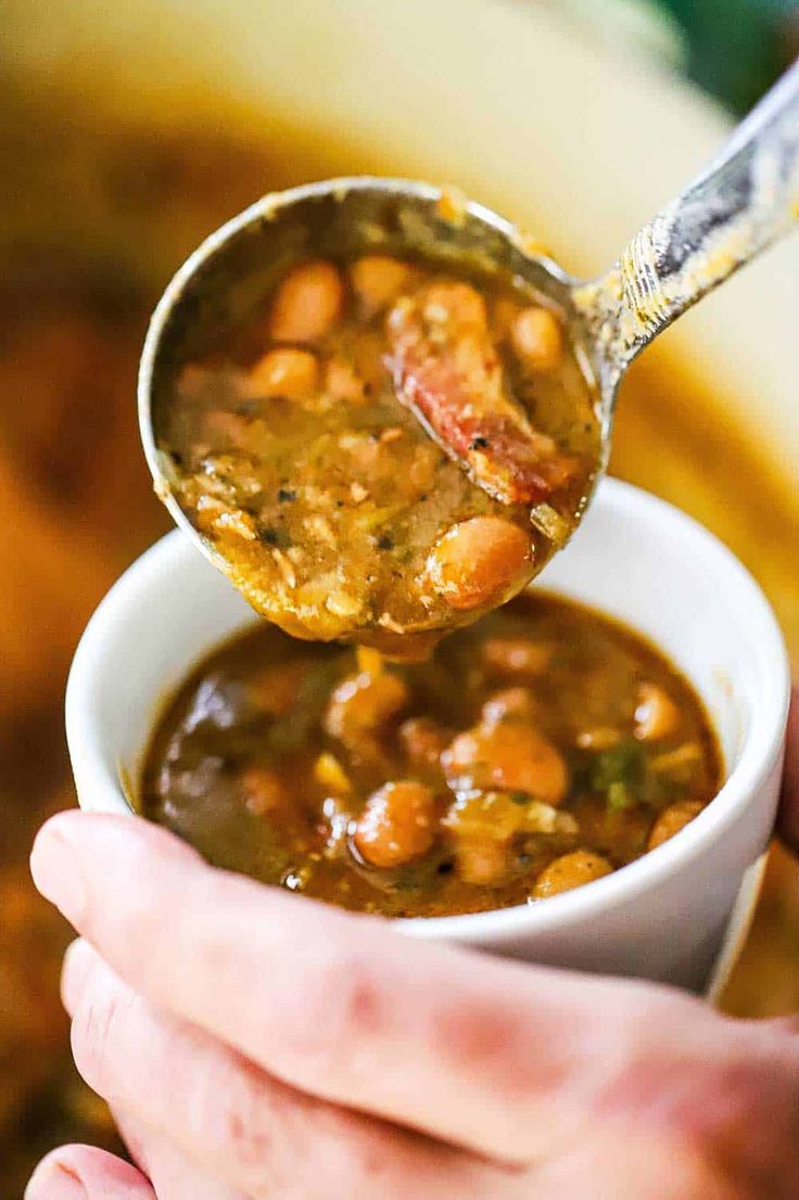 a person holding a spoon full of beans and ham soup