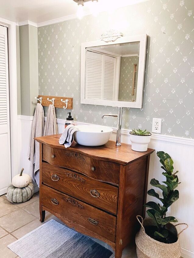 a bathroom sink sitting on top of a wooden dresser next to a mirror and potted plant