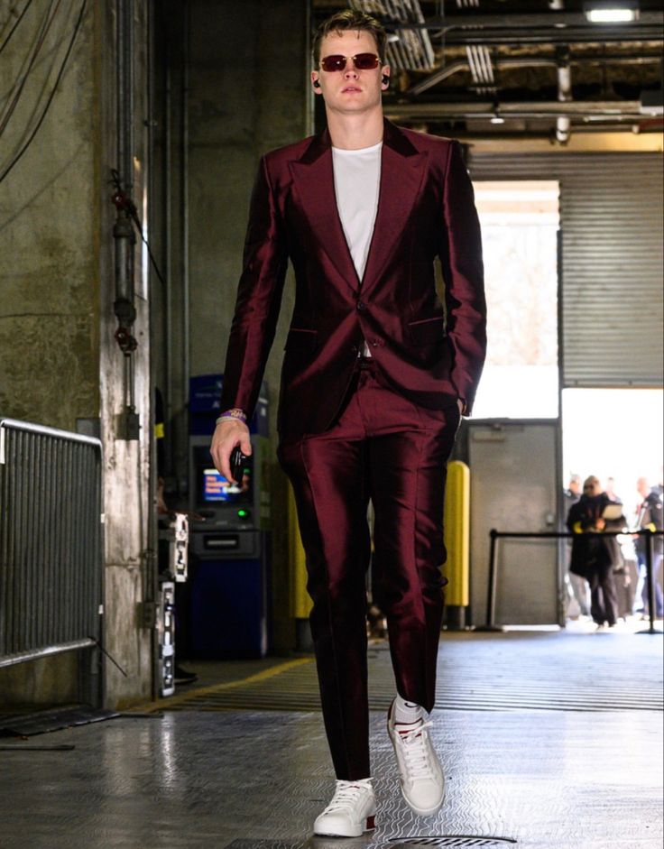 a man in a red suit and white sneakers walking down a runway with his hand on his hip