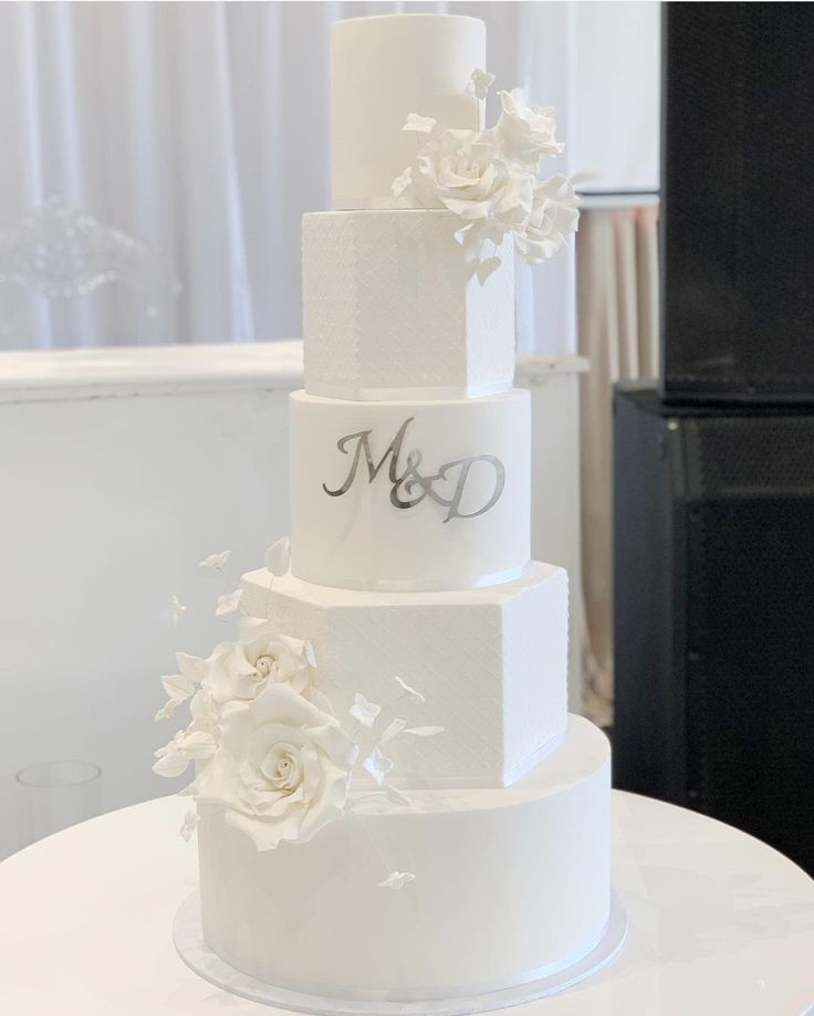 a three tiered wedding cake with white flowers on the top and monogramming