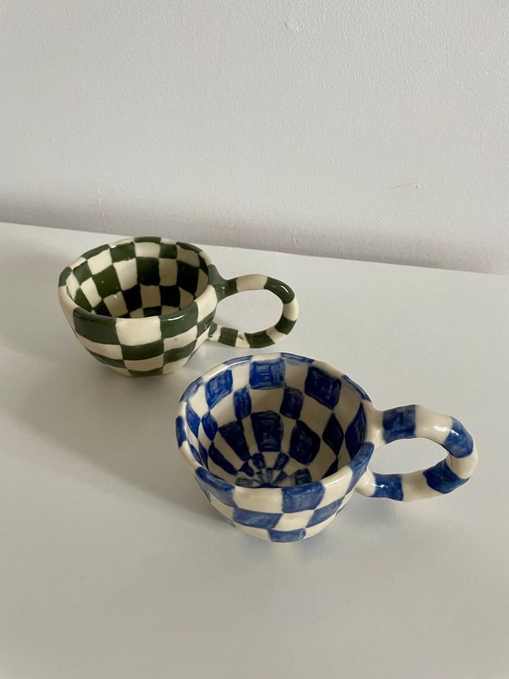 two checkered cups sitting on top of a white table next to each other and one is empty