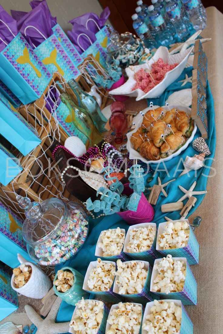 a table topped with lots of food and desserts on top of blue cloth covered tables