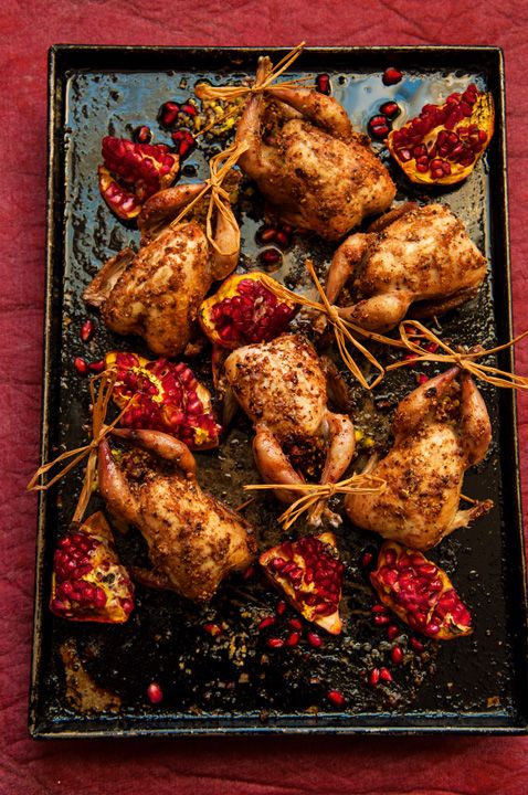 roasted chicken with pomegranates and herbs on a black tray over a red tablecloth