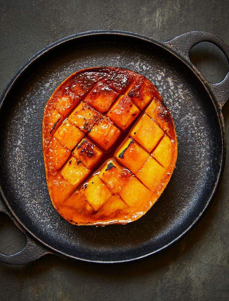 a grilled piece of food on a black plate with tongs next to it