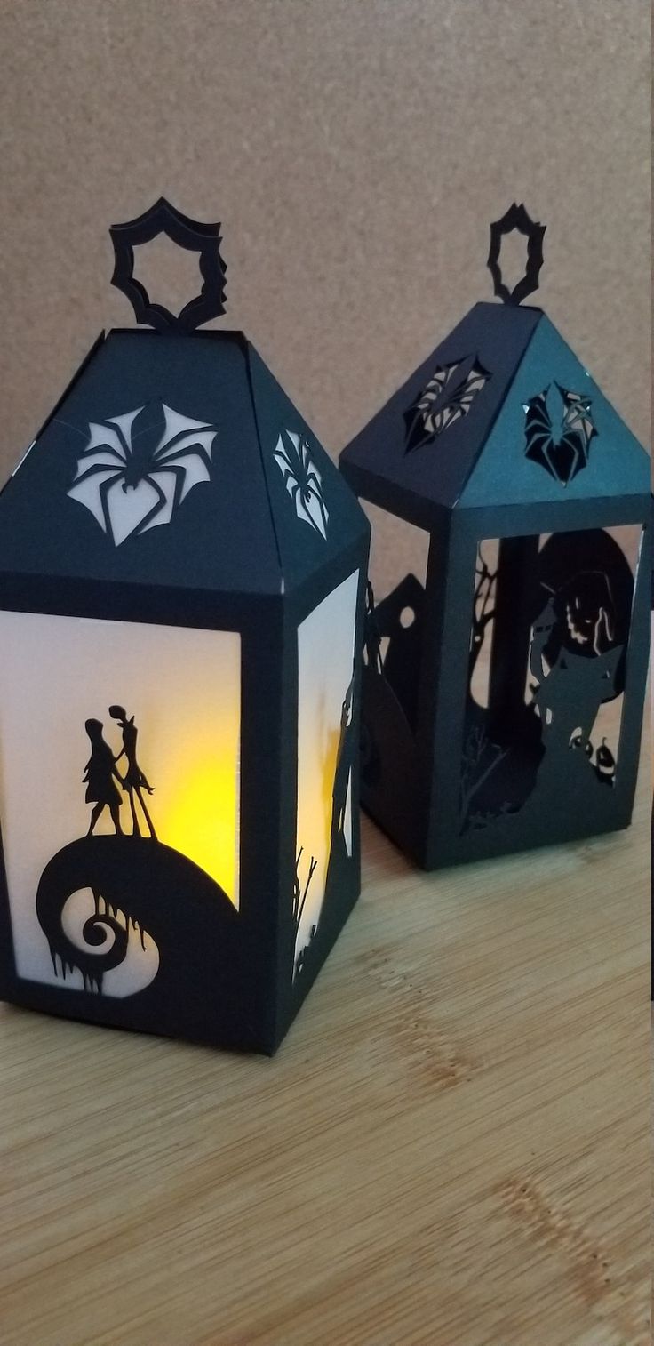 two small black and white lanterns on a wooden table with paper cut outs in the shape of houses