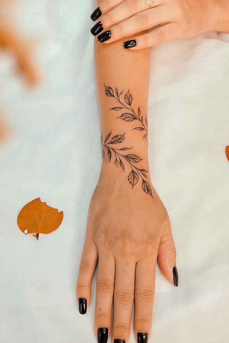 a woman's hand with black nail polish and tattoos on her left arm, next to an orange leaf