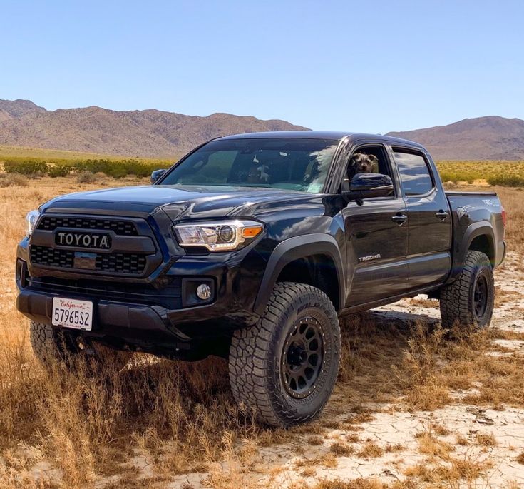 a black toyota pickup truck parked in the middle of a dry grass field with mountains in the background