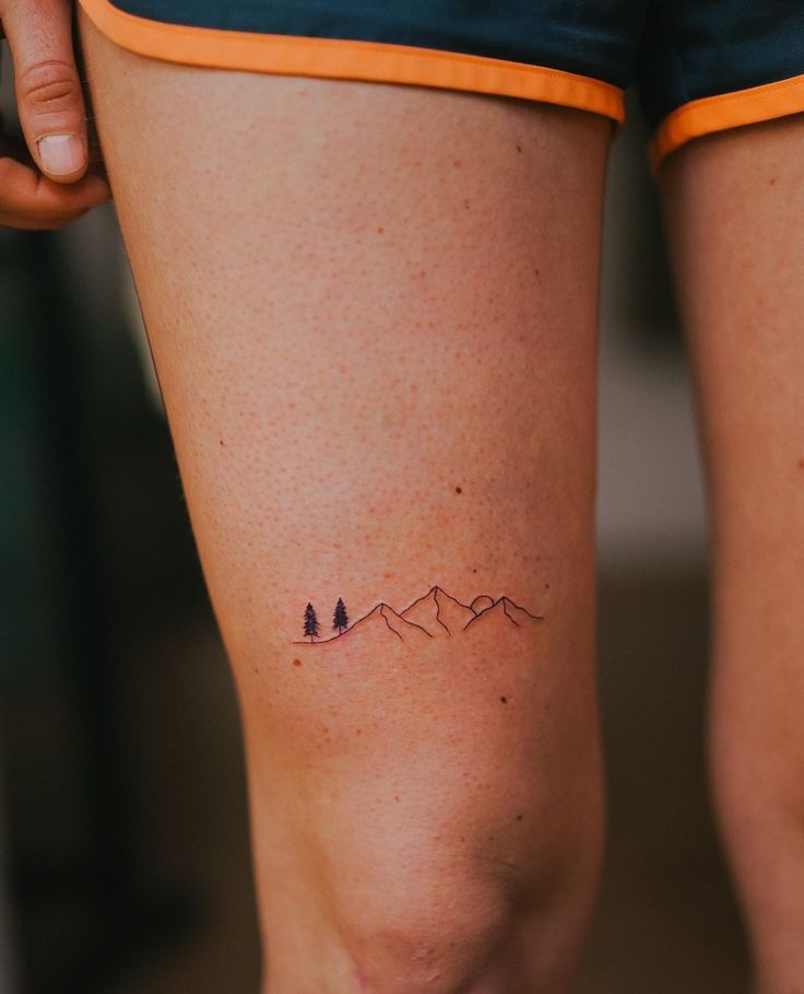 a woman's legs with small tattoos on them and mountains in the back ground