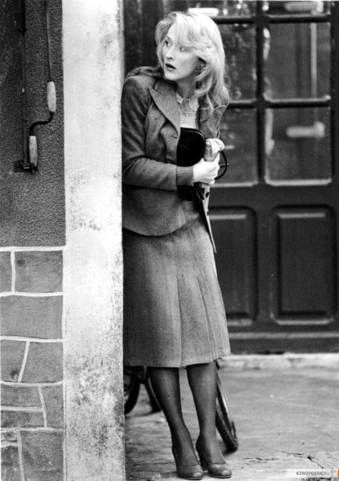 an old black and white photo of a woman leaning against a building with her arms crossed