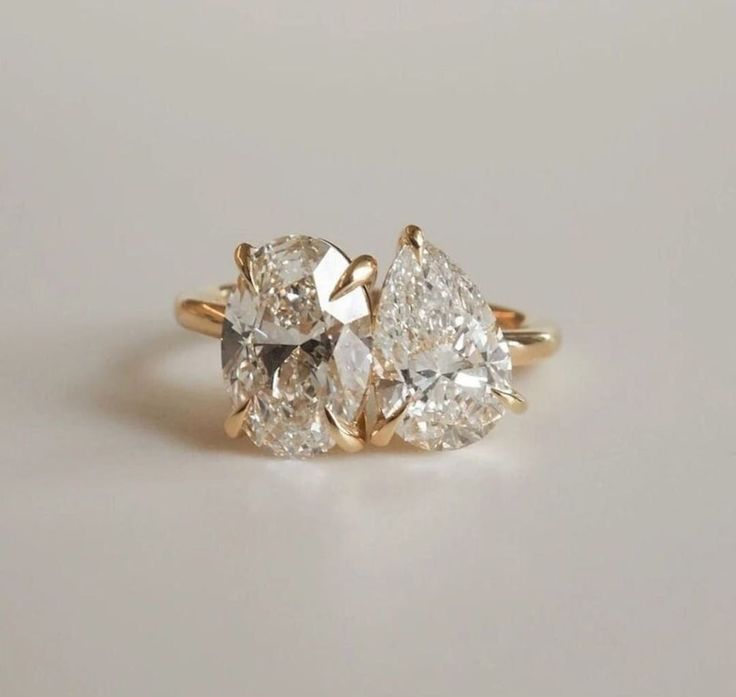 two pear shaped diamond engagement rings on a white surface with the top one in yellow gold