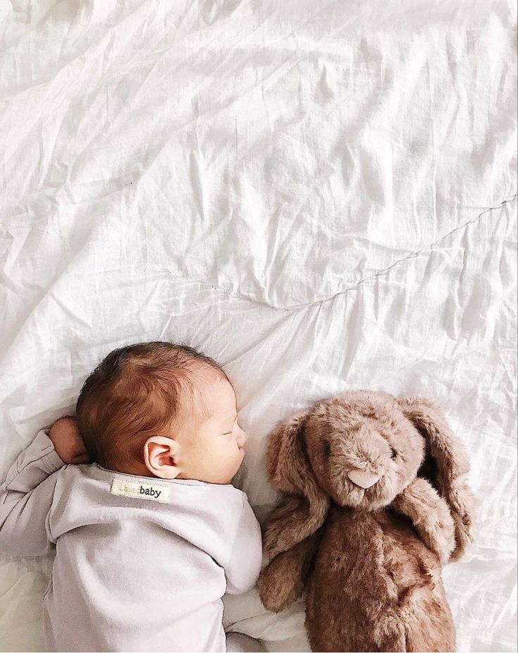 a baby laying on top of a bed next to a stuffed animal bunny rabbit toy