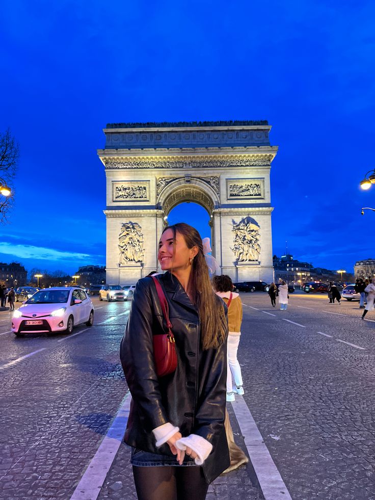 a woman is standing in front of the arc de trioes at night with her hand on her hip