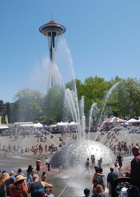 people are gathered around the water fountain in front of space needle, seattle's tallest observation tower